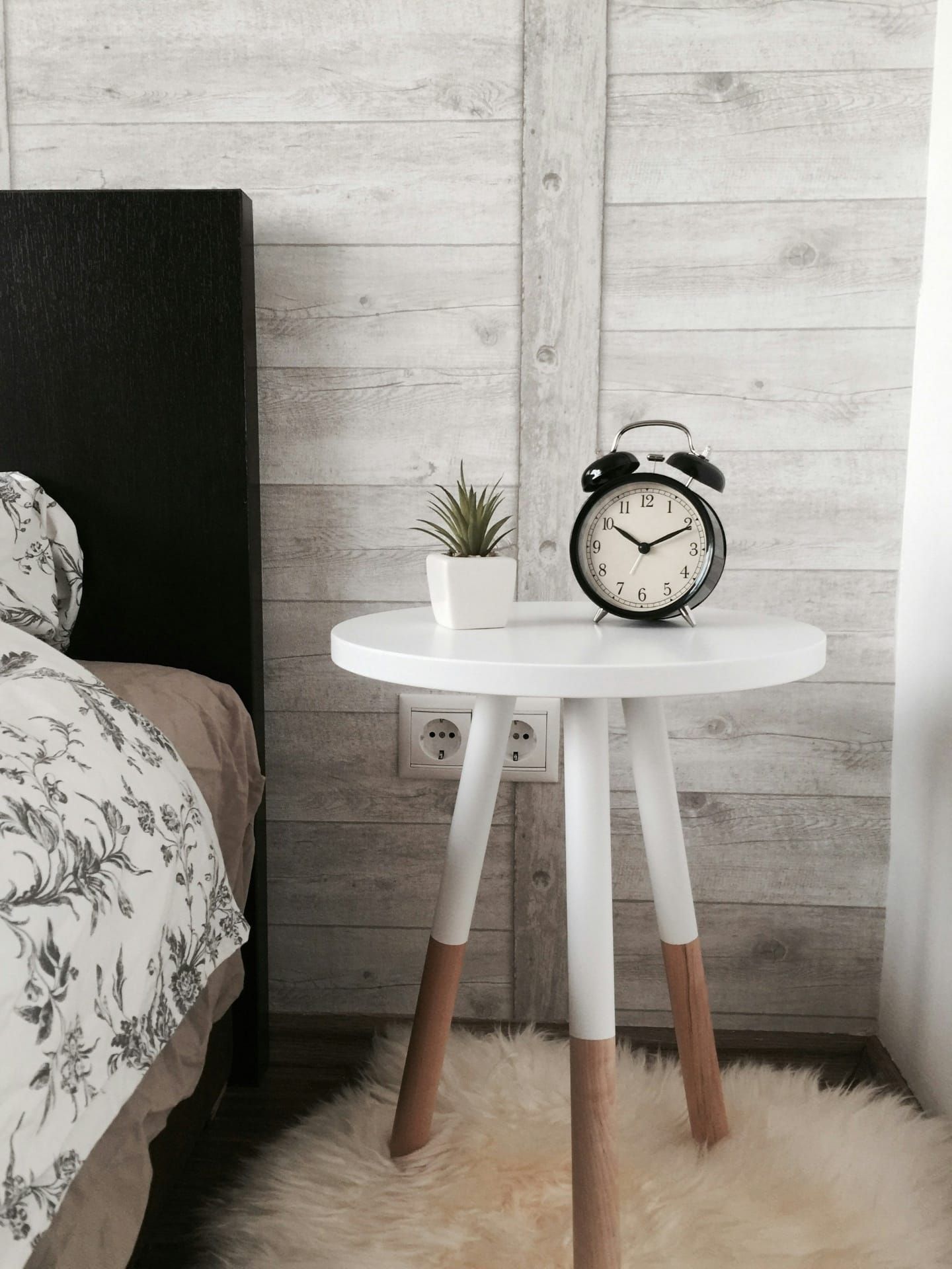 Nachttisch mit Wecker und Pflanze neben einem Bett