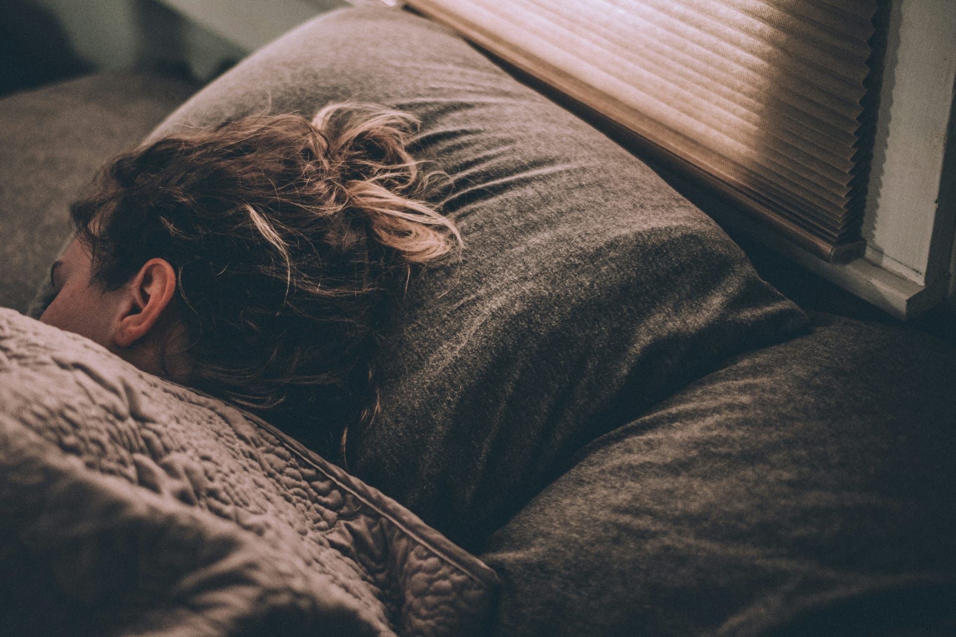 Schlafende Person im Bett mit Kissen und Decke im Morgenlicht